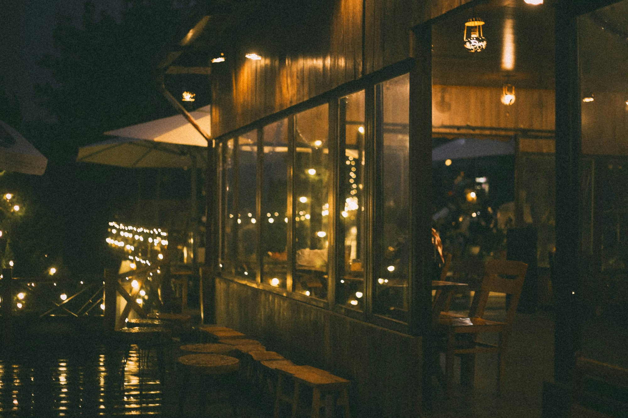 A warmly lit restaurant exterior reflected on rain-dark pavement at night