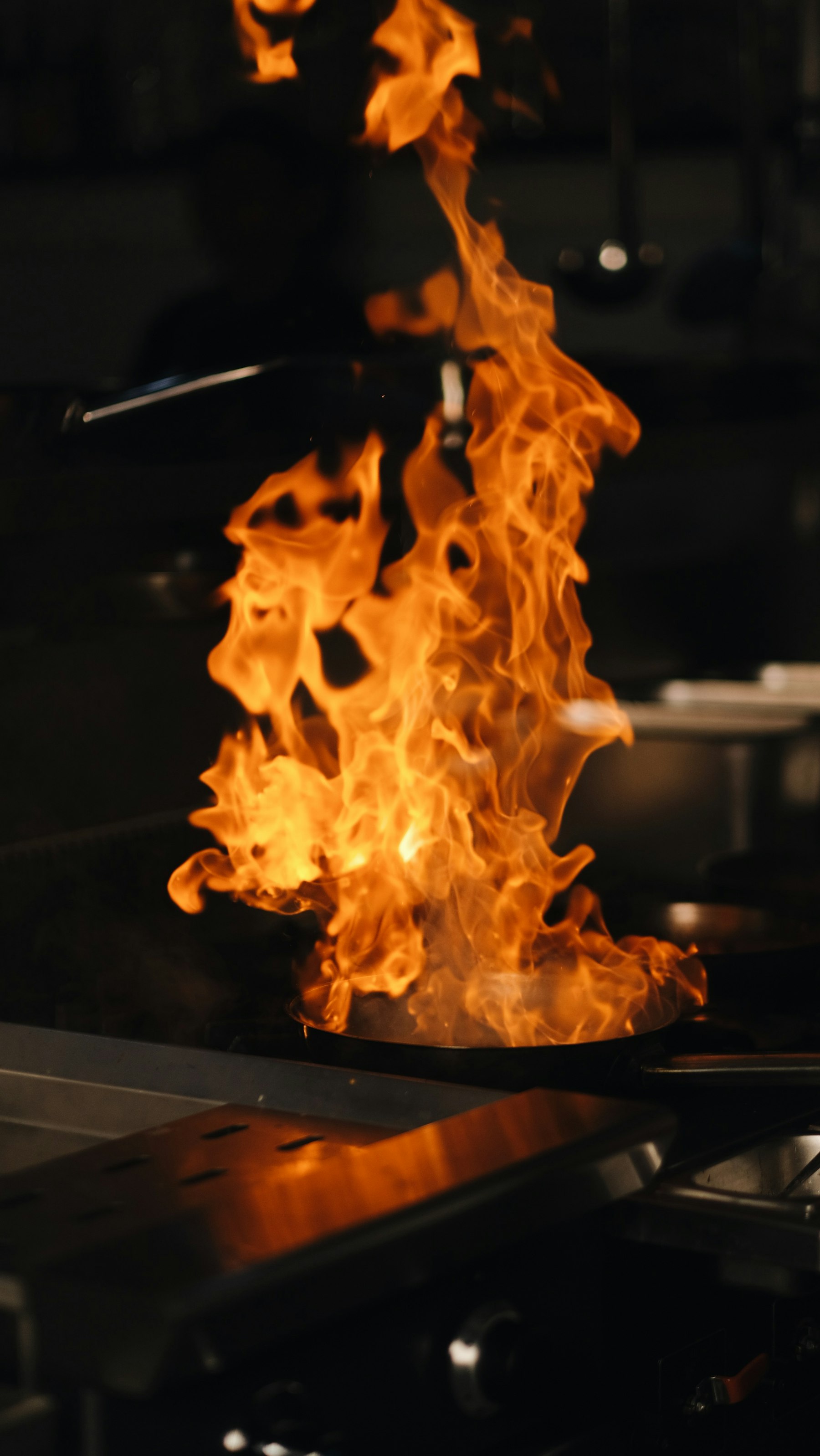 A chef working beside a bright flame in an open restaurant kitchen